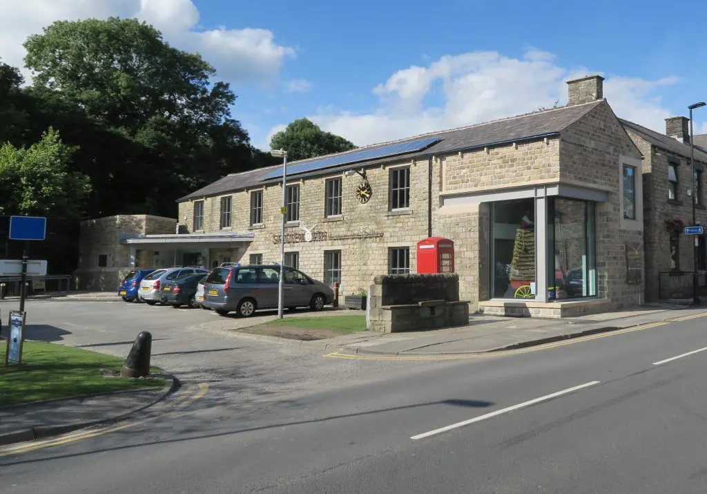 Stone building with car park and red postbox under blue sky with white clouds.