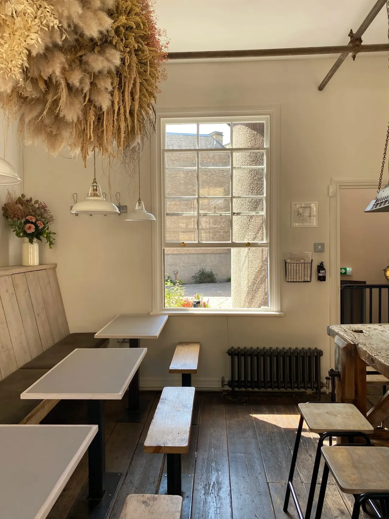 Café interior with bench seating, wooden tables, pendant lights, and dried flower arrangement hanging from ceiling.