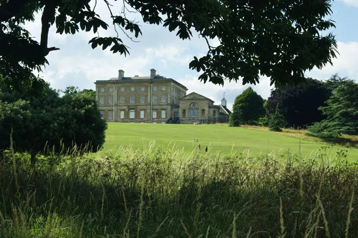 Historic stone manor house set in parkland with manicured lawns and mature trees framing the view.