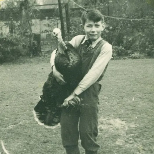 Young boy holding a large dark chicken on a farm yard.