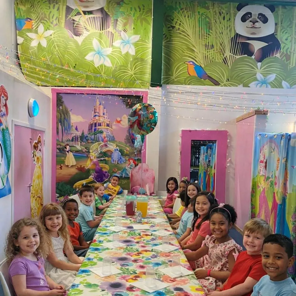 Children seated at a long table during a party in a colourfully decorated hall with jungle and castle themed wall murals.
