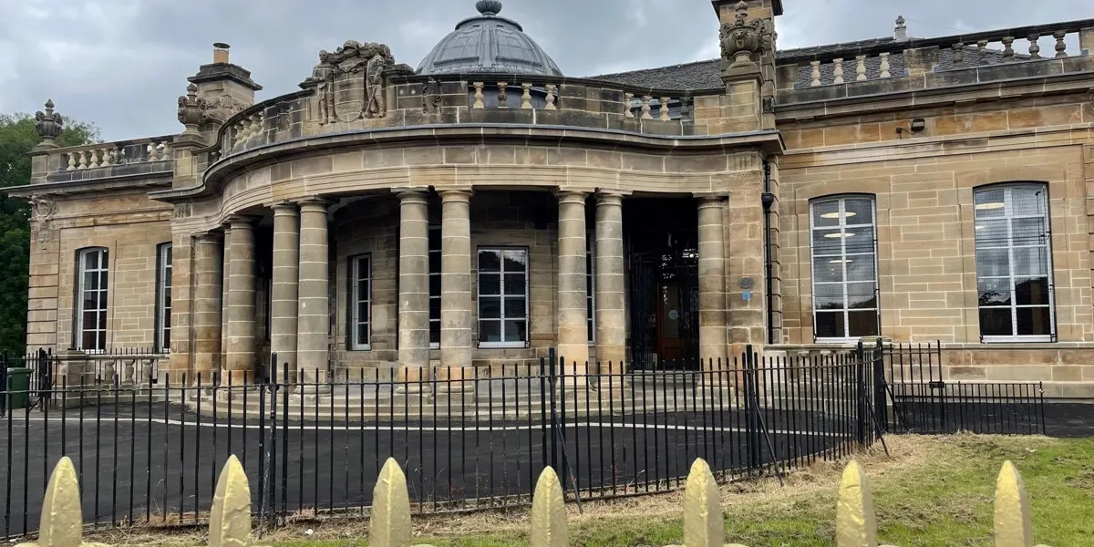 Historic stone library building with columns and dome, surrounded by black railings and stone posts.