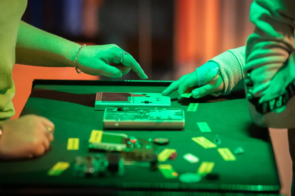 Two visitors with gloved hands assembling electronic components under green lighting at an interactive exhibit.