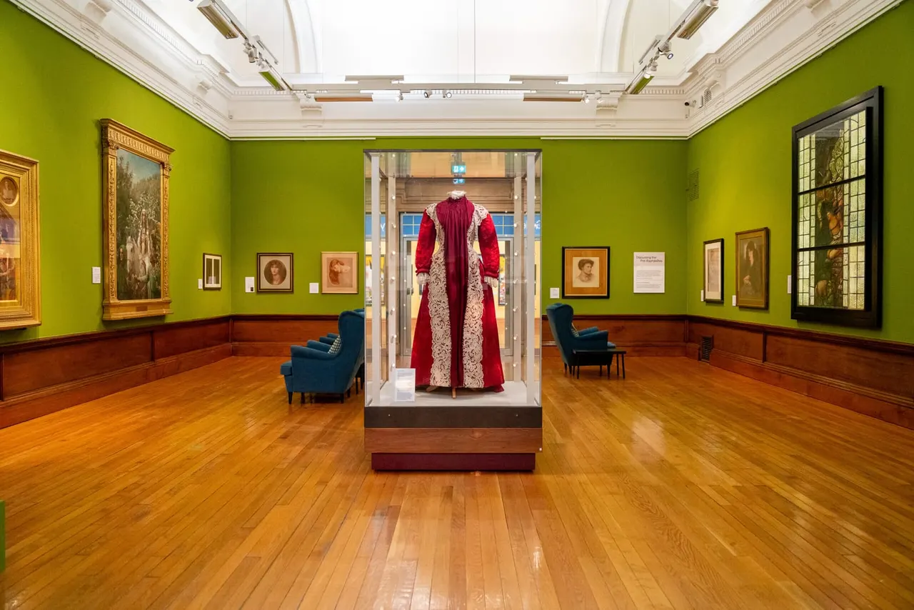 Museum gallery with bright lime-green walls displaying historical portraits and a central display case featuring a red and cream formal robe on a mannequin.