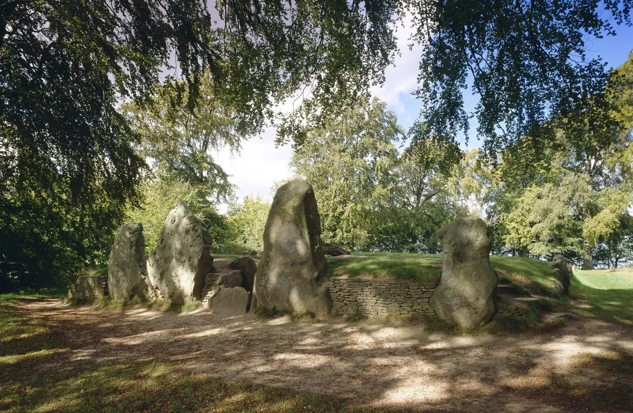 Ancient stone burial chamber with standing stones and earthen mound surrounded by trees.