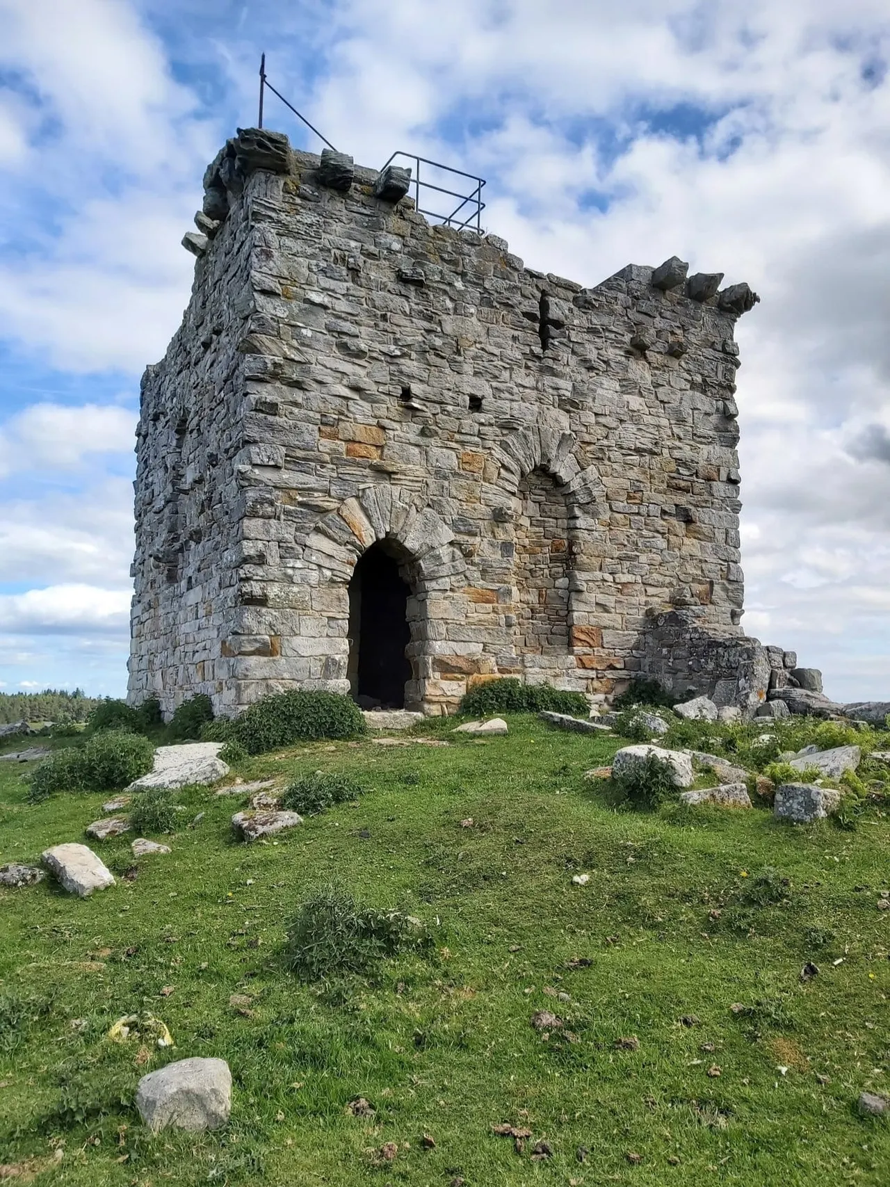 Ancient stone tower ruins with crenellations standing on grassy moorland under cloudy sky.