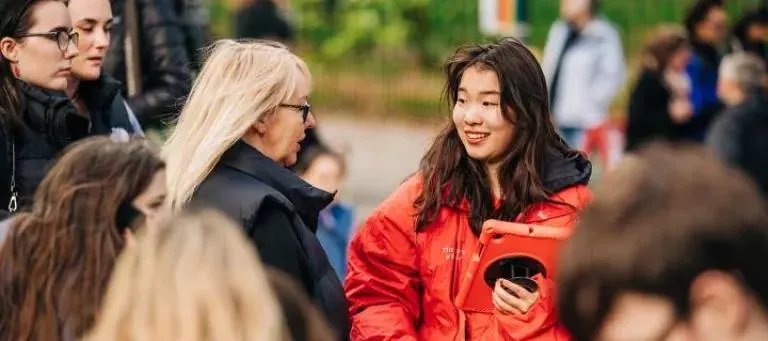 A staff member in a red jacket talks with visitors outdoors at a geological venue.
