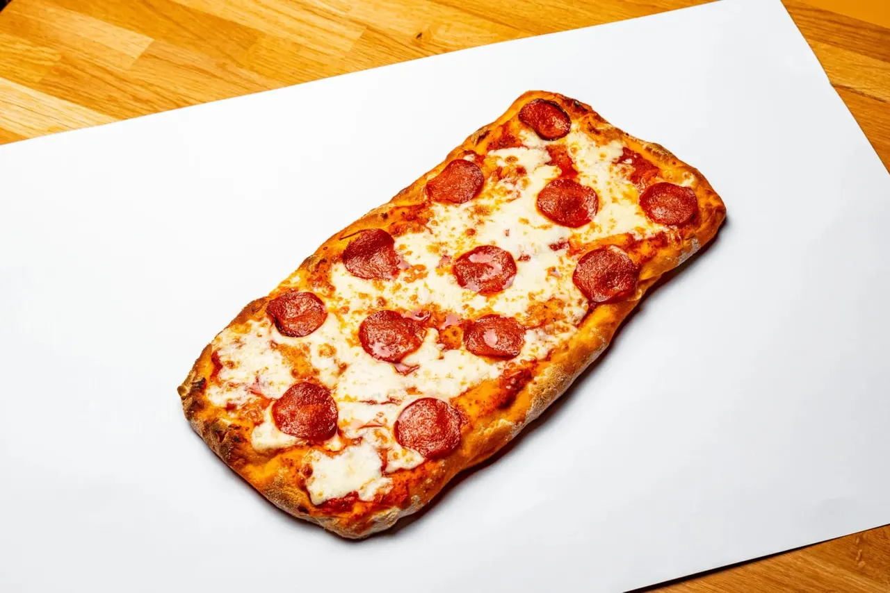 Rectangular pepperoni pizza on white paper over wooden surface.