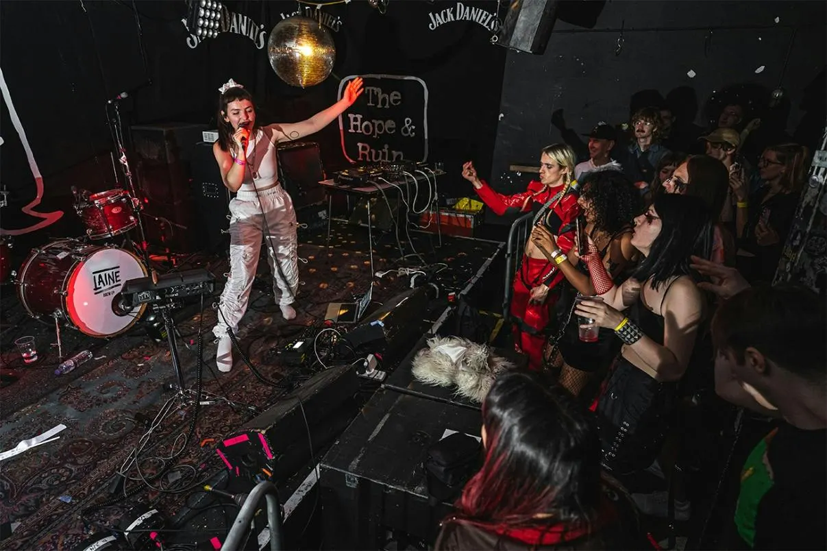 Live band performing on stage to a crowd of enthusiastic dancers in an intimate venue with red lighting.