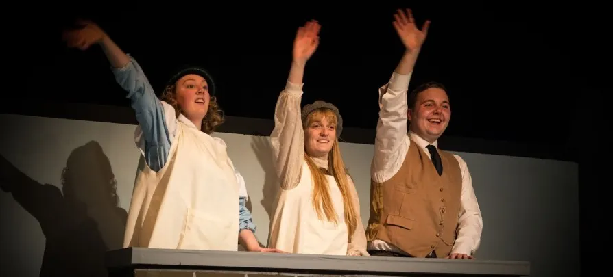 Three performers on stage taking a bow with raised arms during a theatre production.