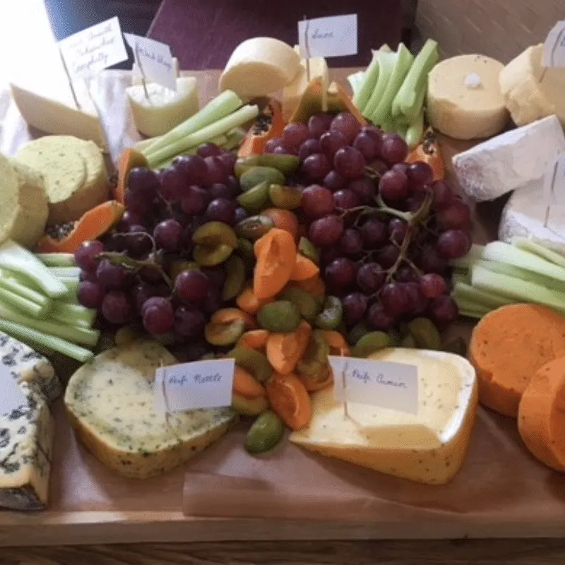 Charcuterie board display with red grapes, cheeses, celery, pickled vegetables and sliced bread with name labels.