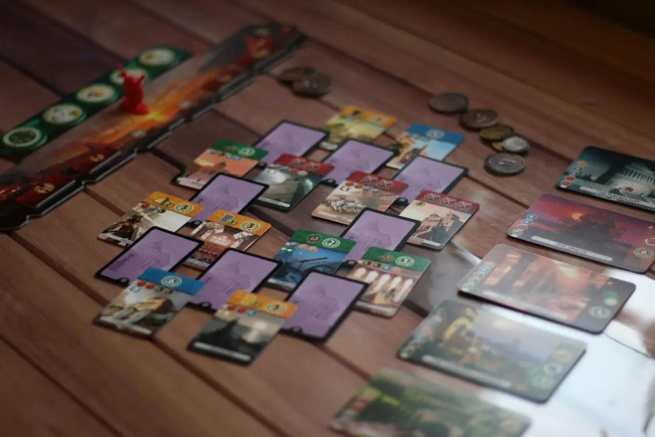 Board game in progress on wooden table with cards, tokens and player pieces arranged during gameplay.