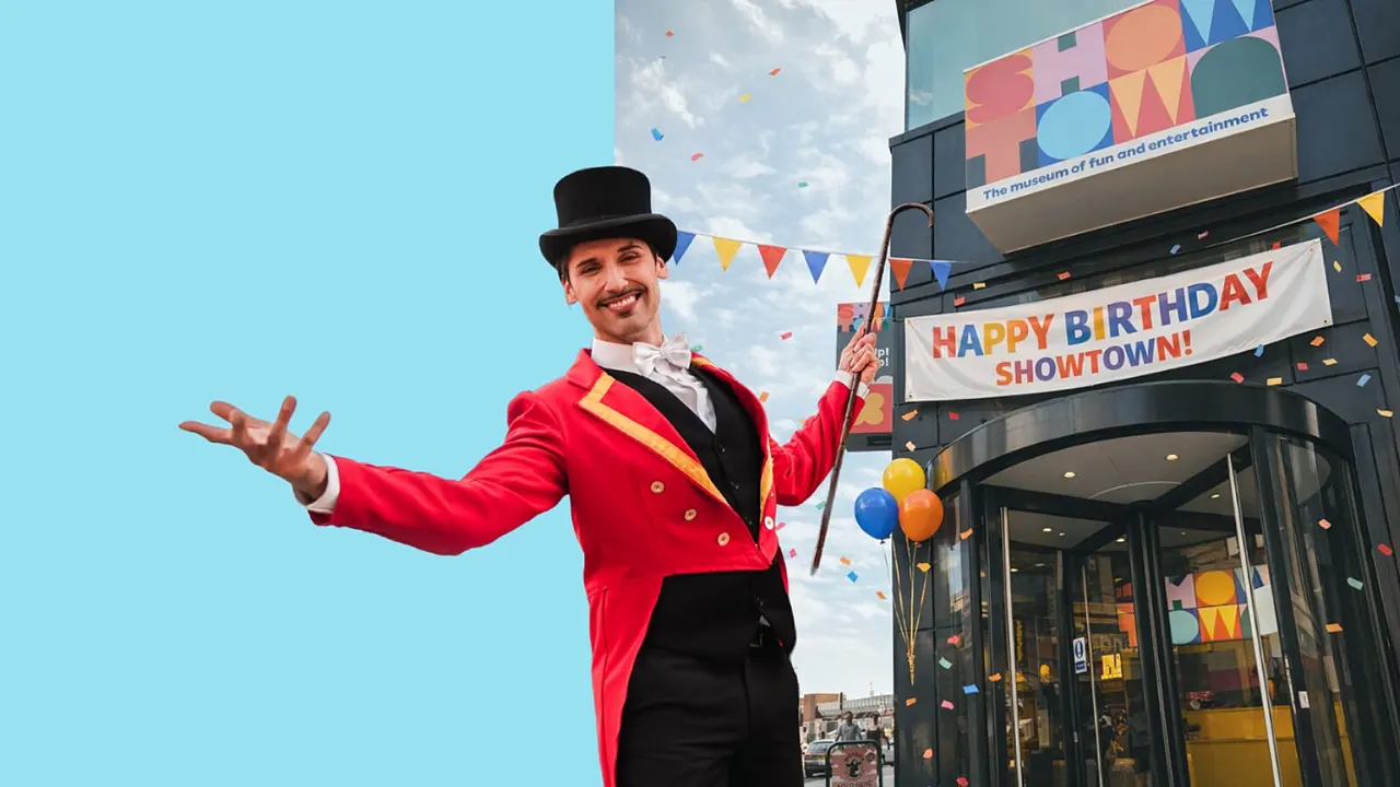 Ringmaster in red tailcoat and top hat poses outside a entertainment venue entrance with confetti falling.
