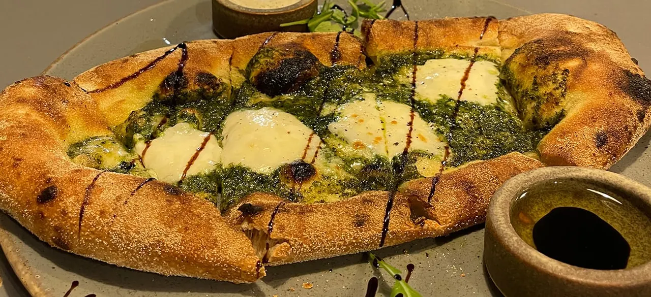 Toasted ciabatta bread topped with melted cheese, pesto and microgreens, served with olive oil for dipping.