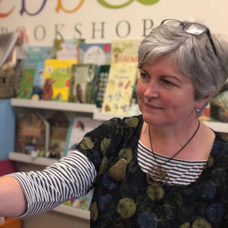Woman with grey hair and glasses on her head browsing children's books on shelves in a bookshop.