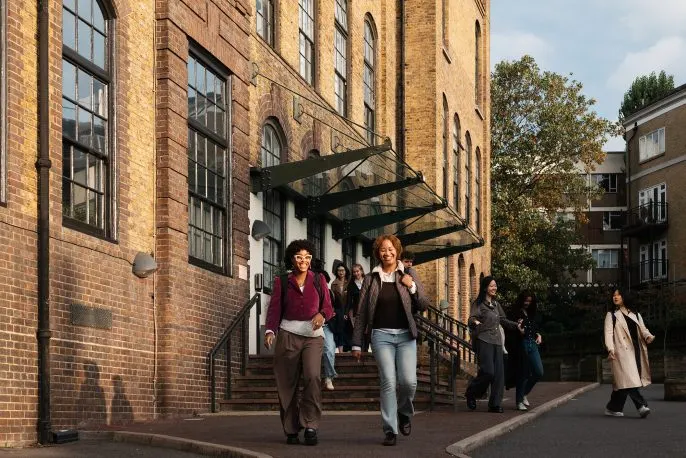 People walking down steps outside a historic brick building with large windows.