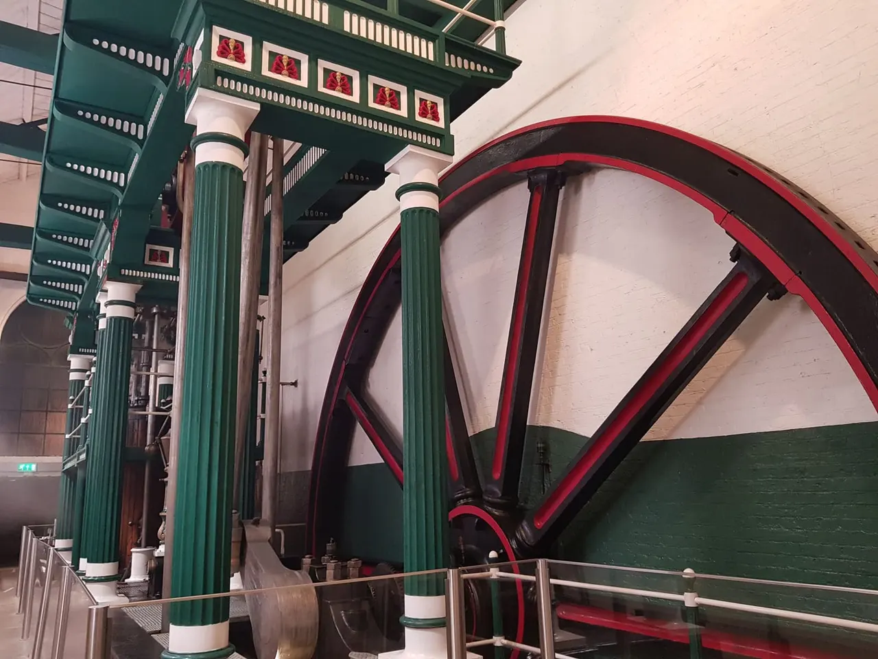 Large red industrial beam engine with green supporting columns on display indoors at a museum.
