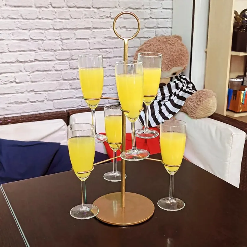 Tiered brass stand displaying yellow juice cocktails and red drinks in champagne flutes on a dark table.