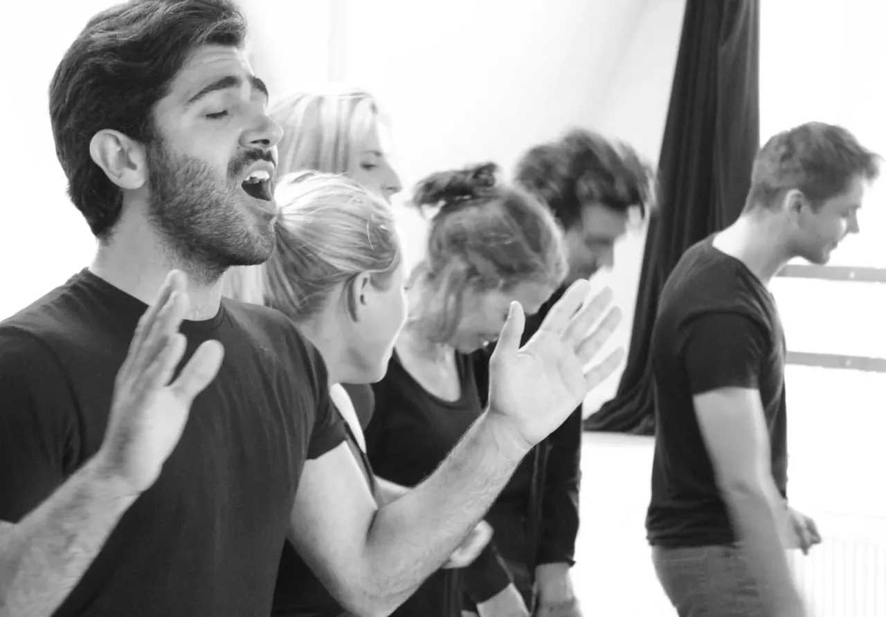 Group of people in black t-shirts singing or performing together indoors.