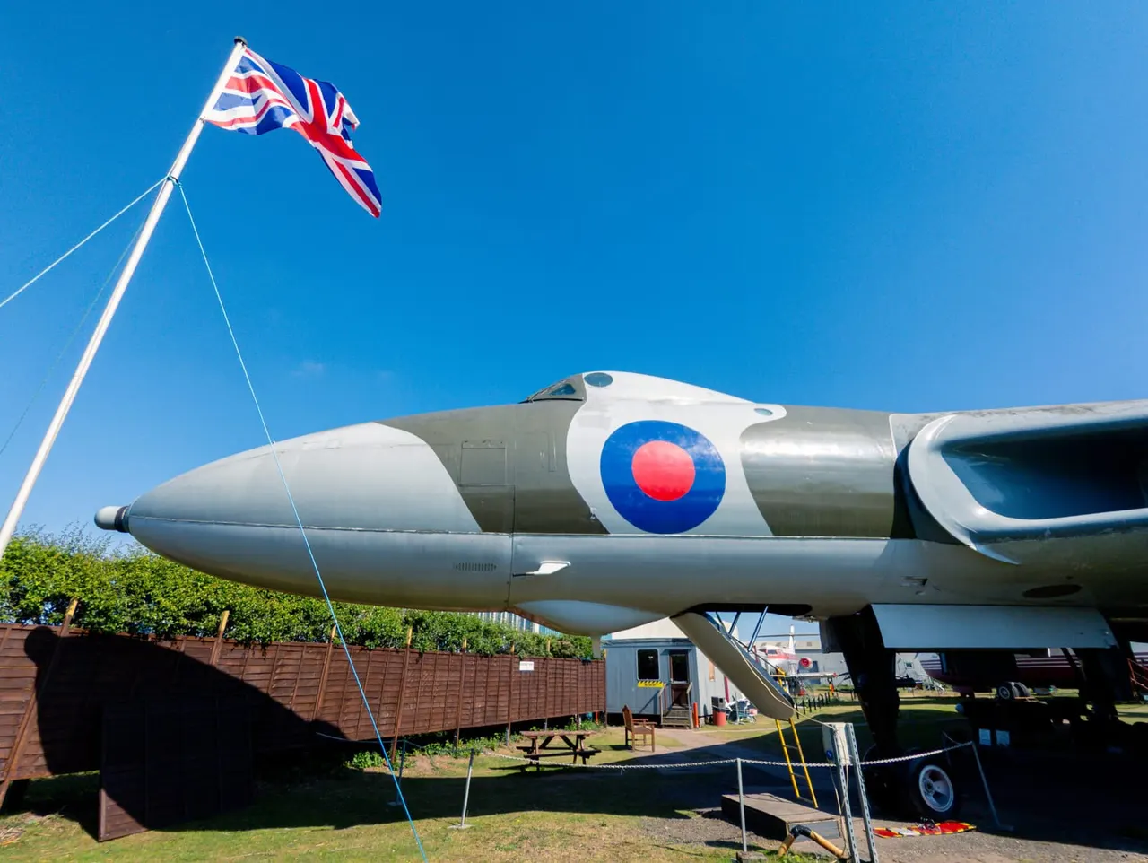 Historic military aircraft with RAF roundel on display under clear blue sky with Union Jack flag.