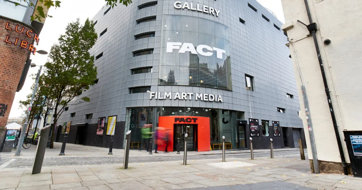 Modern cylindrical building with "Gallery", "Fact" and "Film Art Media" signage, red entrance canopy, and paved plaza forecourt.