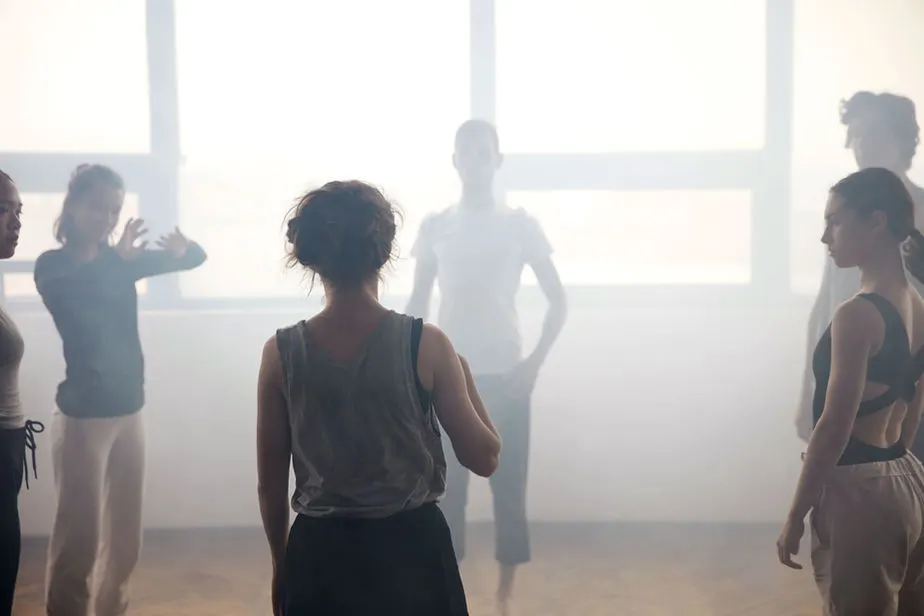 Group fitness class with multiple participants exercising together in a bright, minimalist studio space.