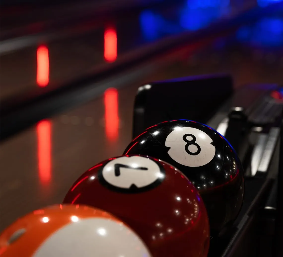 Pool balls numbered 7 and 8 on a pool table with red neon lighting in background.