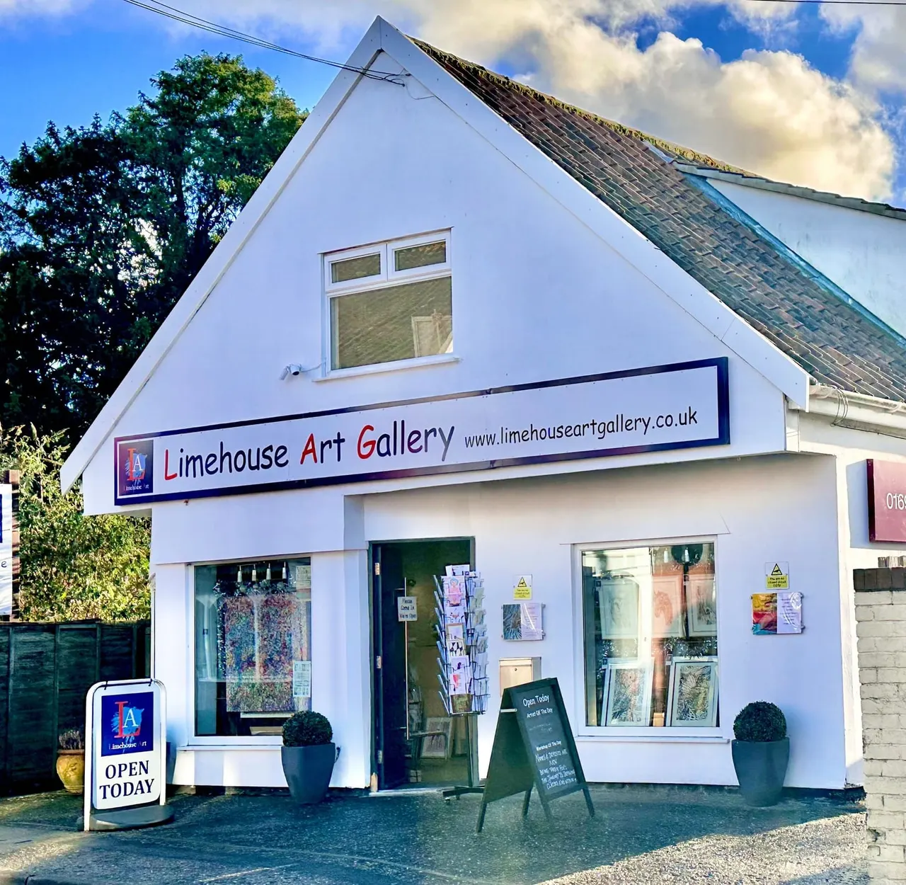 White painted art gallery building with large windows, signage, and an "Open Today" sign outside.