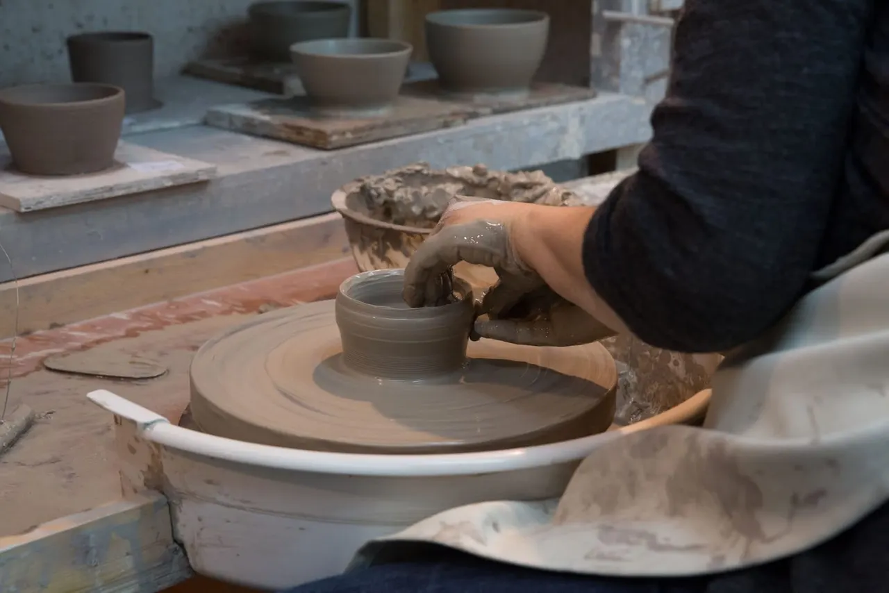 Person shaping wet clay on a pottery wheel in a ceramics studio.