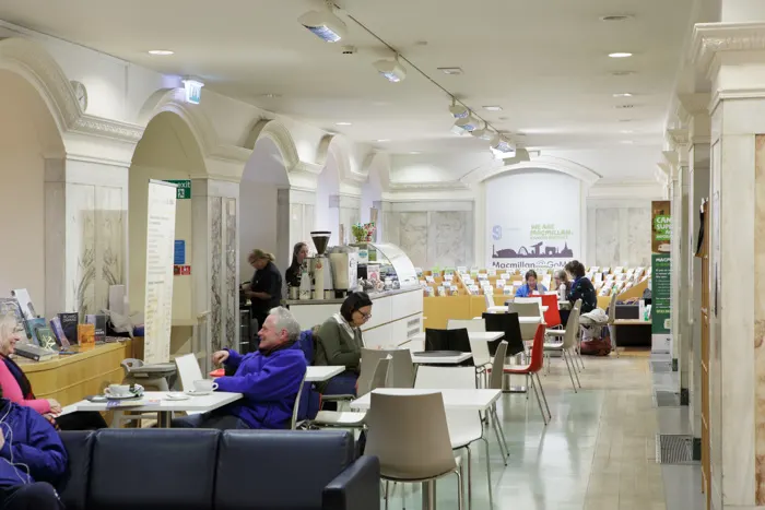 Interior of a bright, modern library with archways, where visitors sit at tables with laptops whilst staff work at a service desk.
