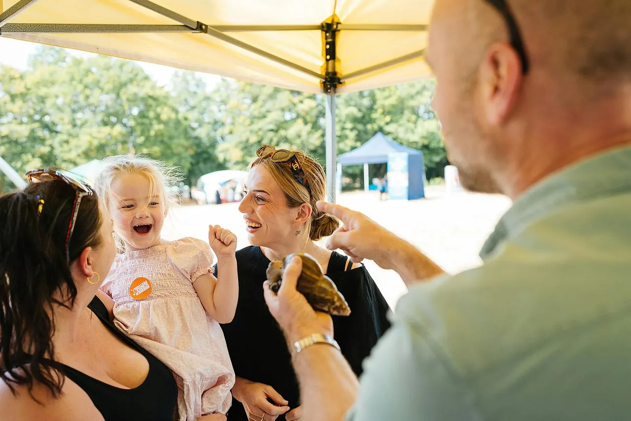 A young child delightedly holds a large bird of prey under a yellow shade tent whilst adults smile nearby at an outdoor event.