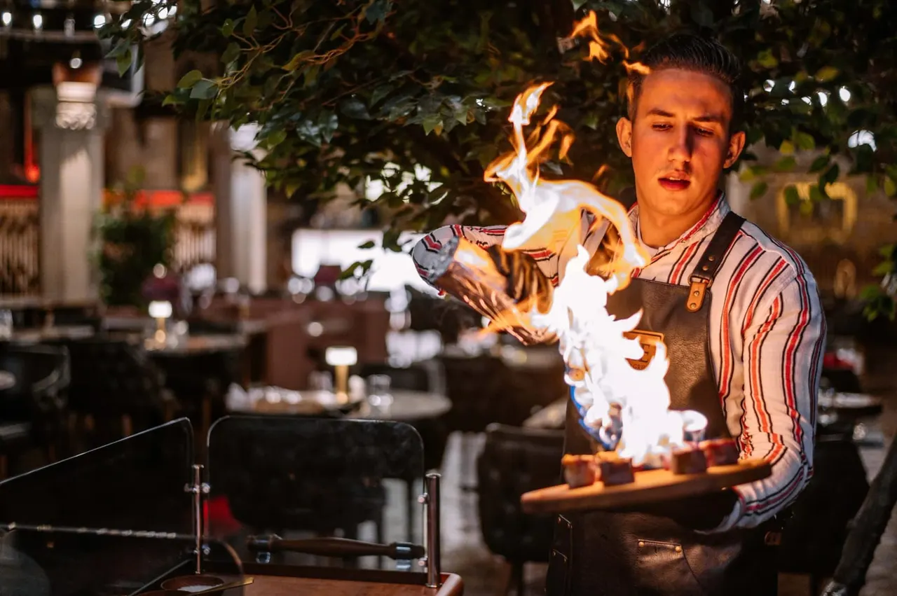 Chef performing flaming tableside cooking demonstration at an outdoor evening dining venue.