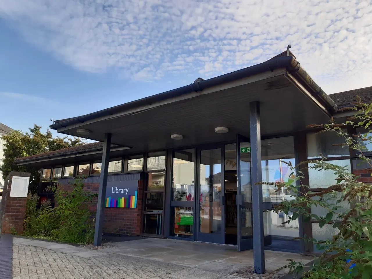 Modern library building with blue frame and glass frontage under blue sky with clouds.