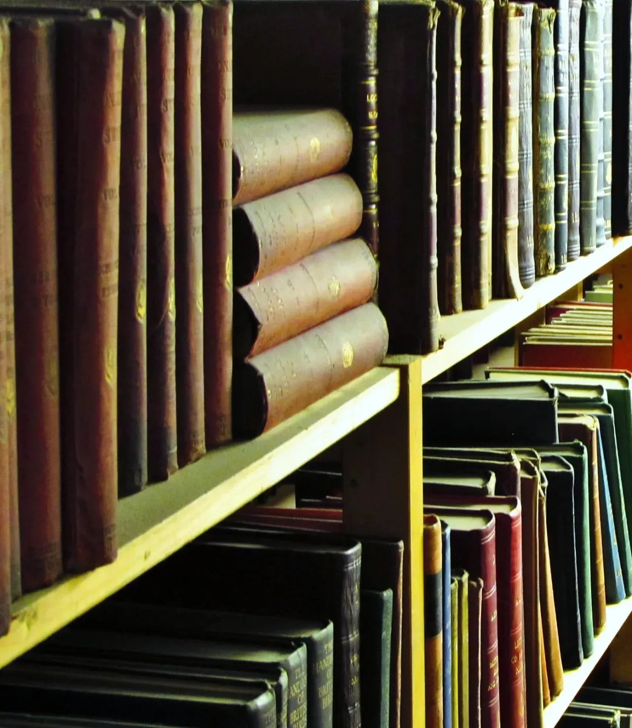 Shelves displaying antique leather-bound books and rolled documents in a library collection.