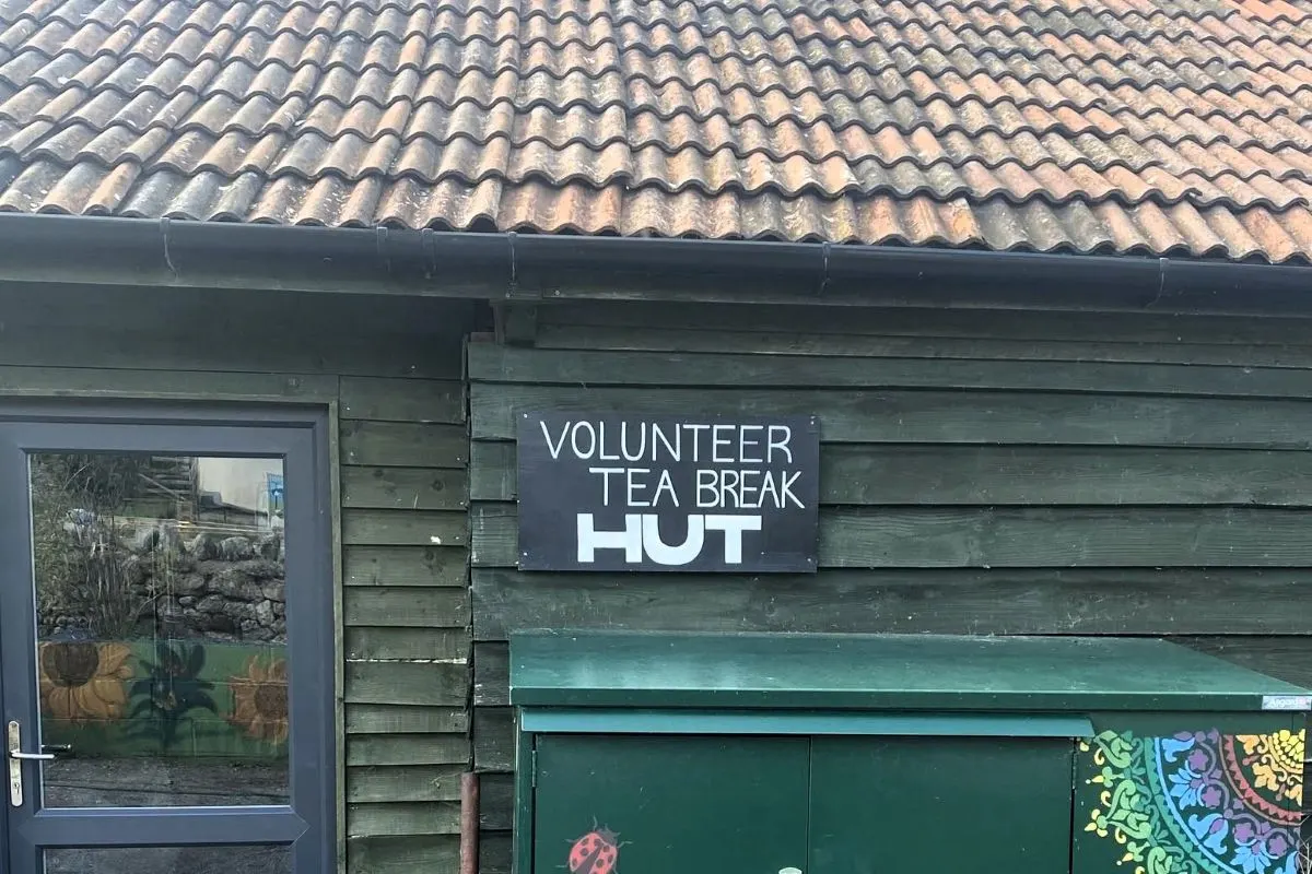 Green wooden hut with "Volunteer Tea Break Hut" sign, terracotta tiled roof above.