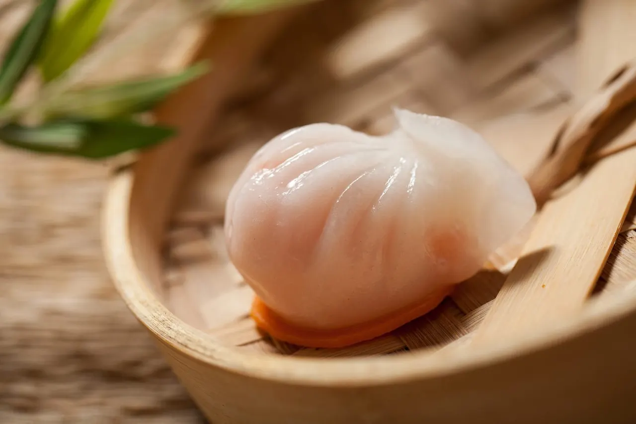 Translucent prawn dumpling on a wooden spoon with spring onion and wooden surface.