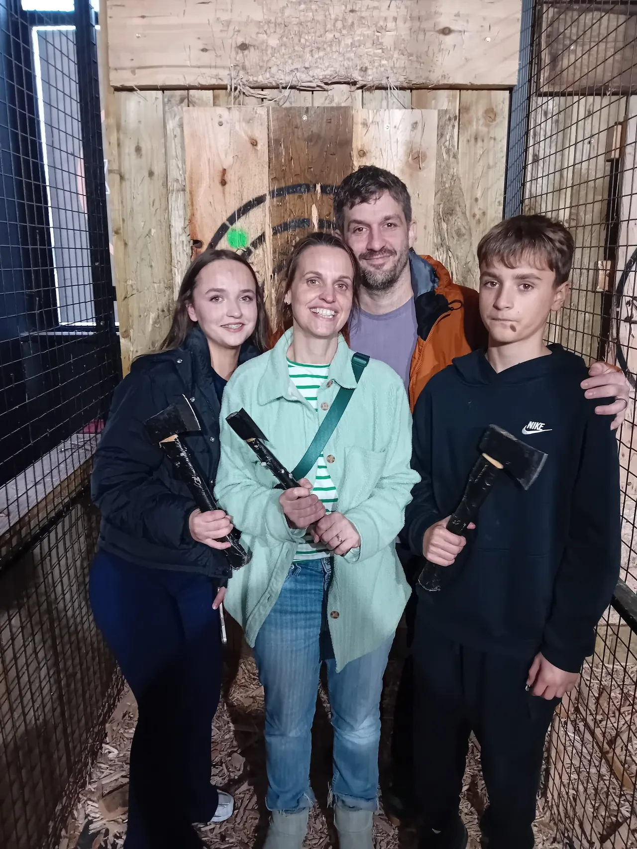 Four people holding axes smile for the camera inside an axe-throwing venue with wooden target boards.
