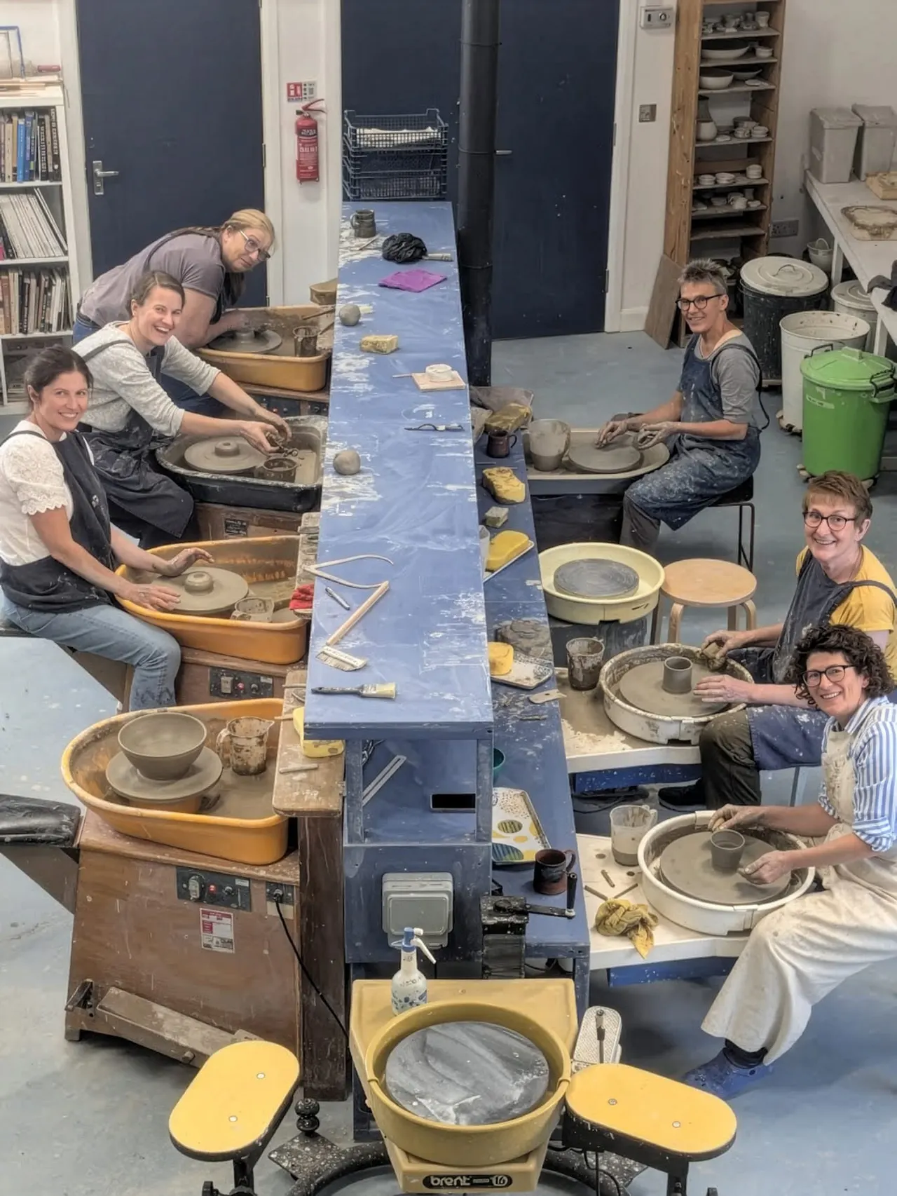 A group of adults working at pottery wheels in a ceramic studio, shaping clay.