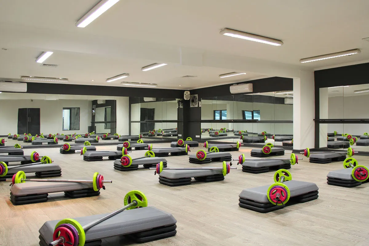 Spacious fitness studio with multiple step platforms and barbells with bright neon-yellow and pink weight plates arranged across wooden flooring.
