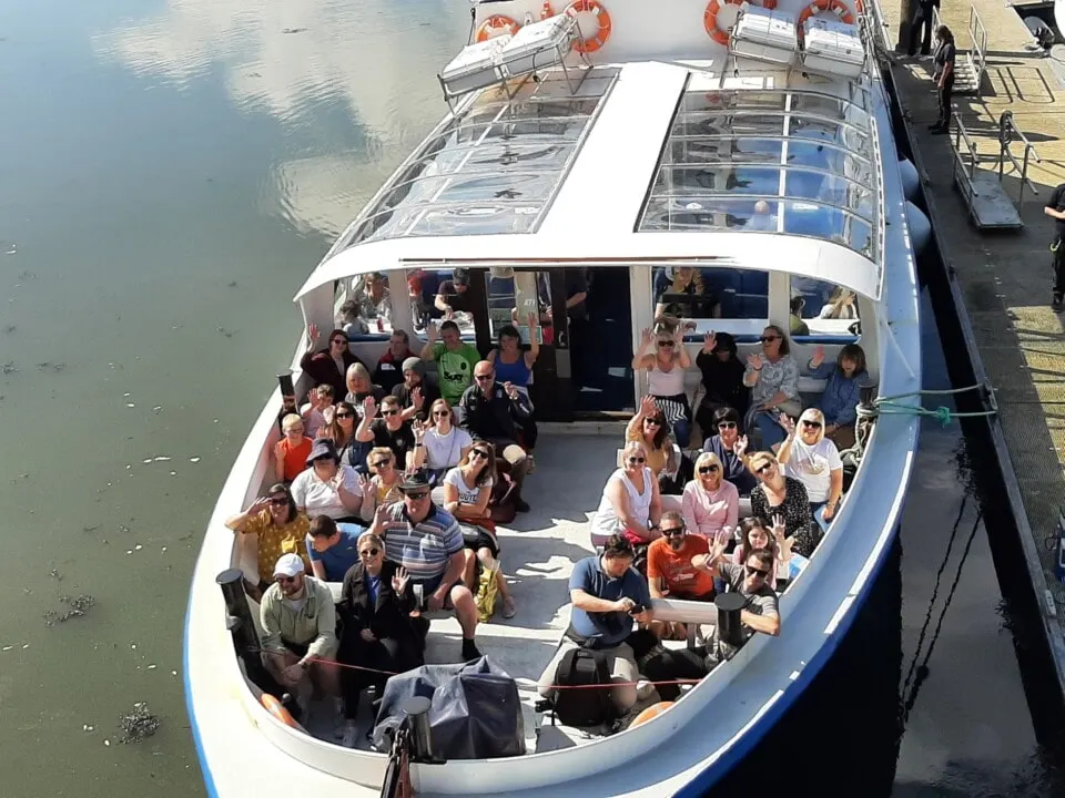 Overhead view of a full passenger boat docked at a pier with numerous tourists seated and standing on deck.