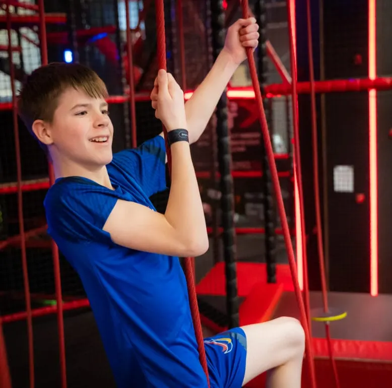 Child climbing red rope structure in indoor play gym with neon lighting.