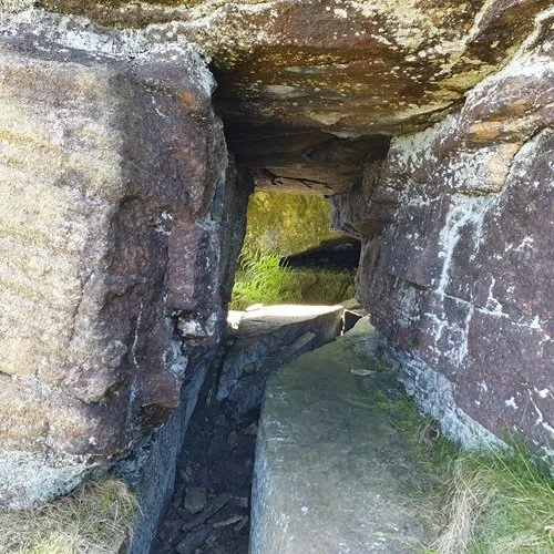Stone passageway with moss-covered walls leading through narrow ancient rock formation.