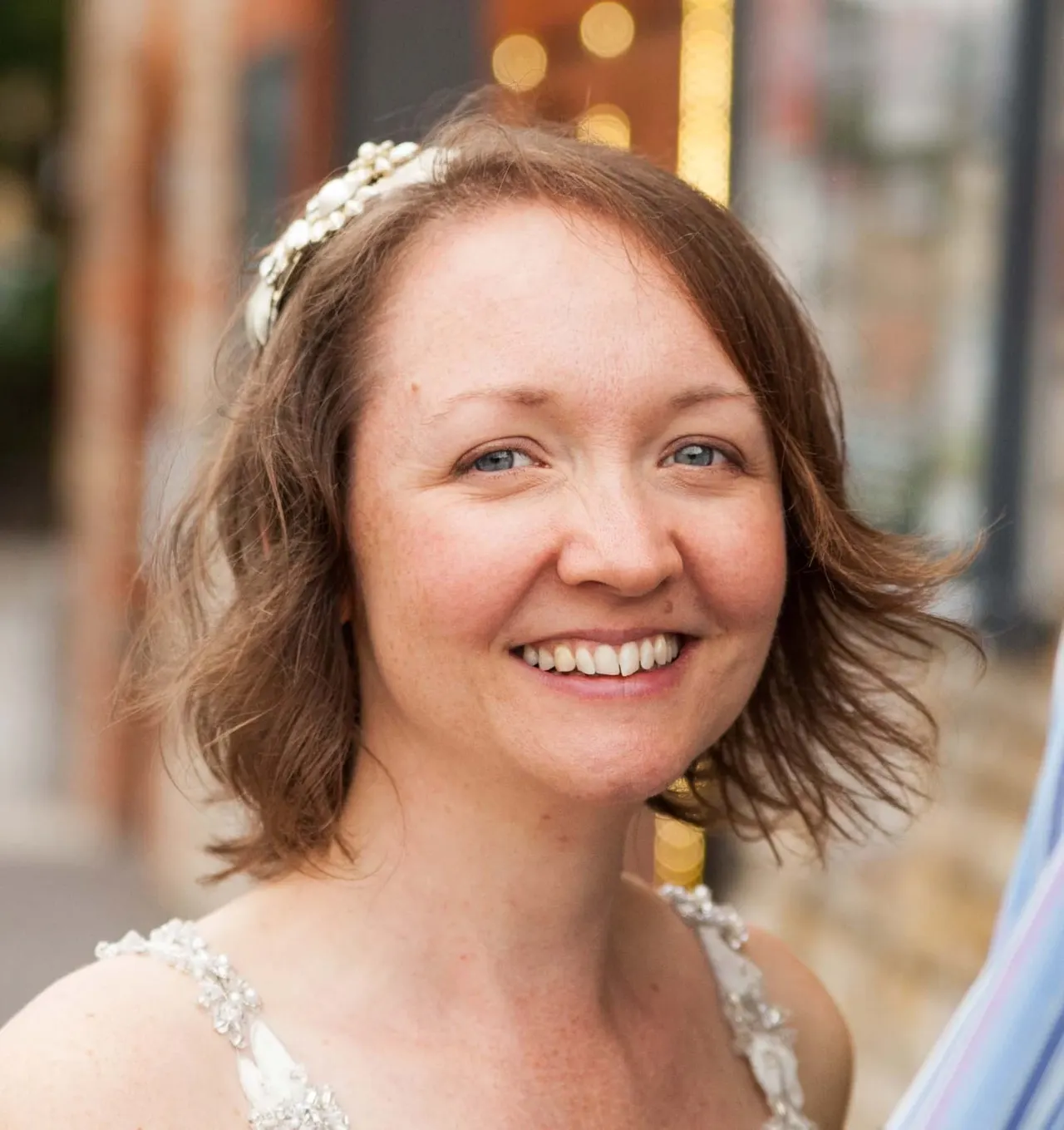 Woman wearing a pearl headpiece and embellished white dress, smiling at the camera outdoors.