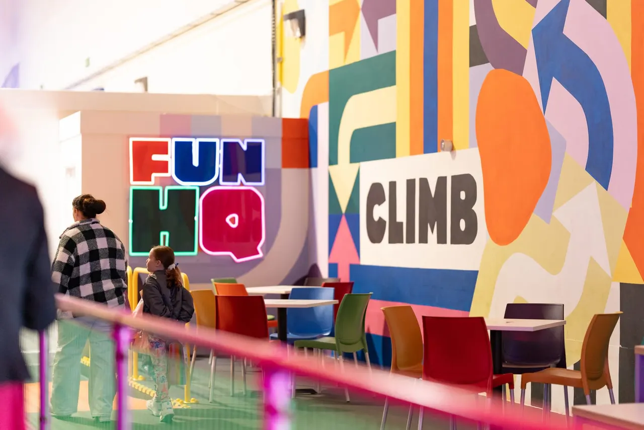 A child sits at a colourful table inside an indoor play centre with vibrant neon signage and geometric wall art.