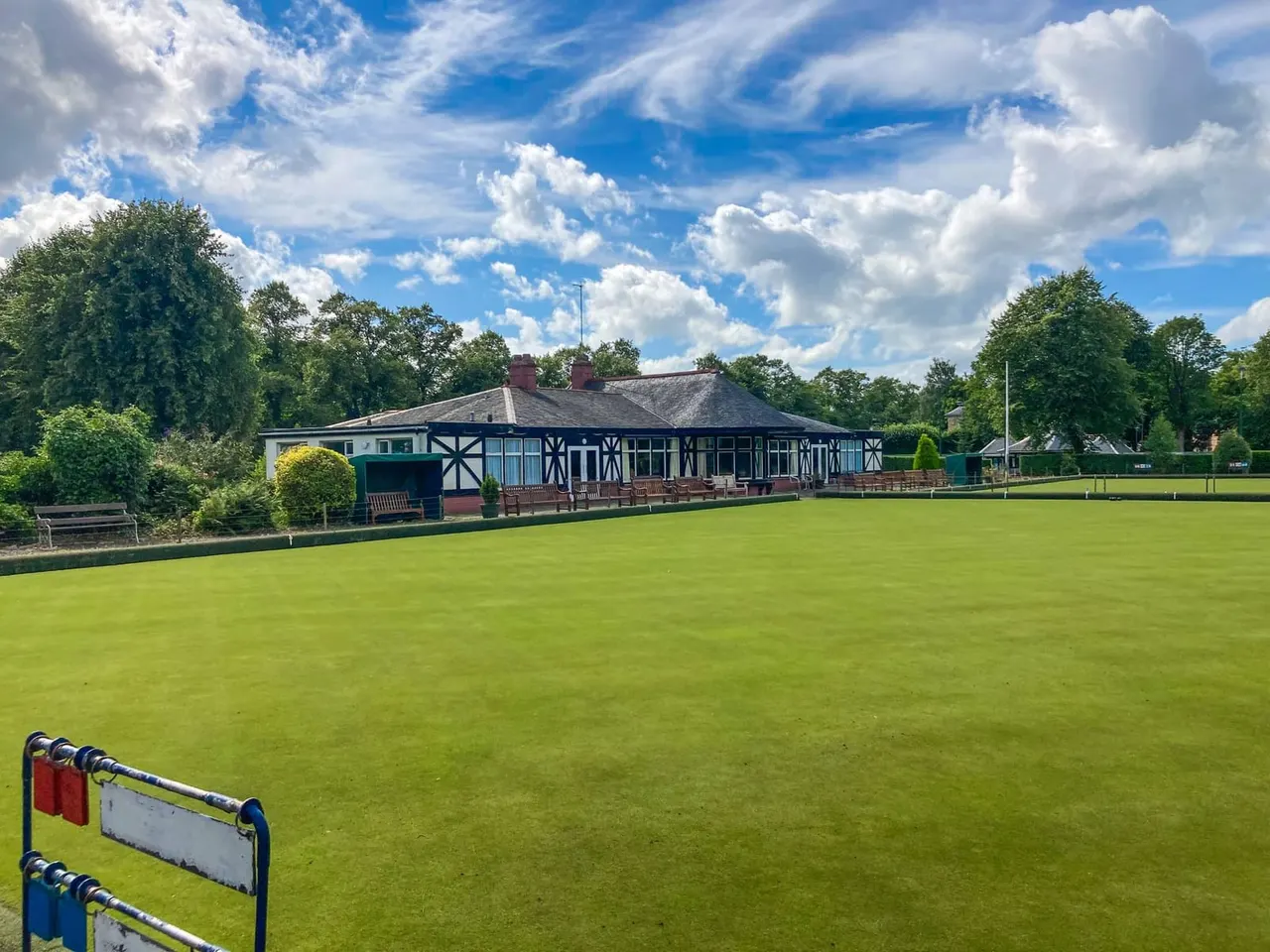 A bowling green with a half-timbered clubhouse under blue sky with white clouds.