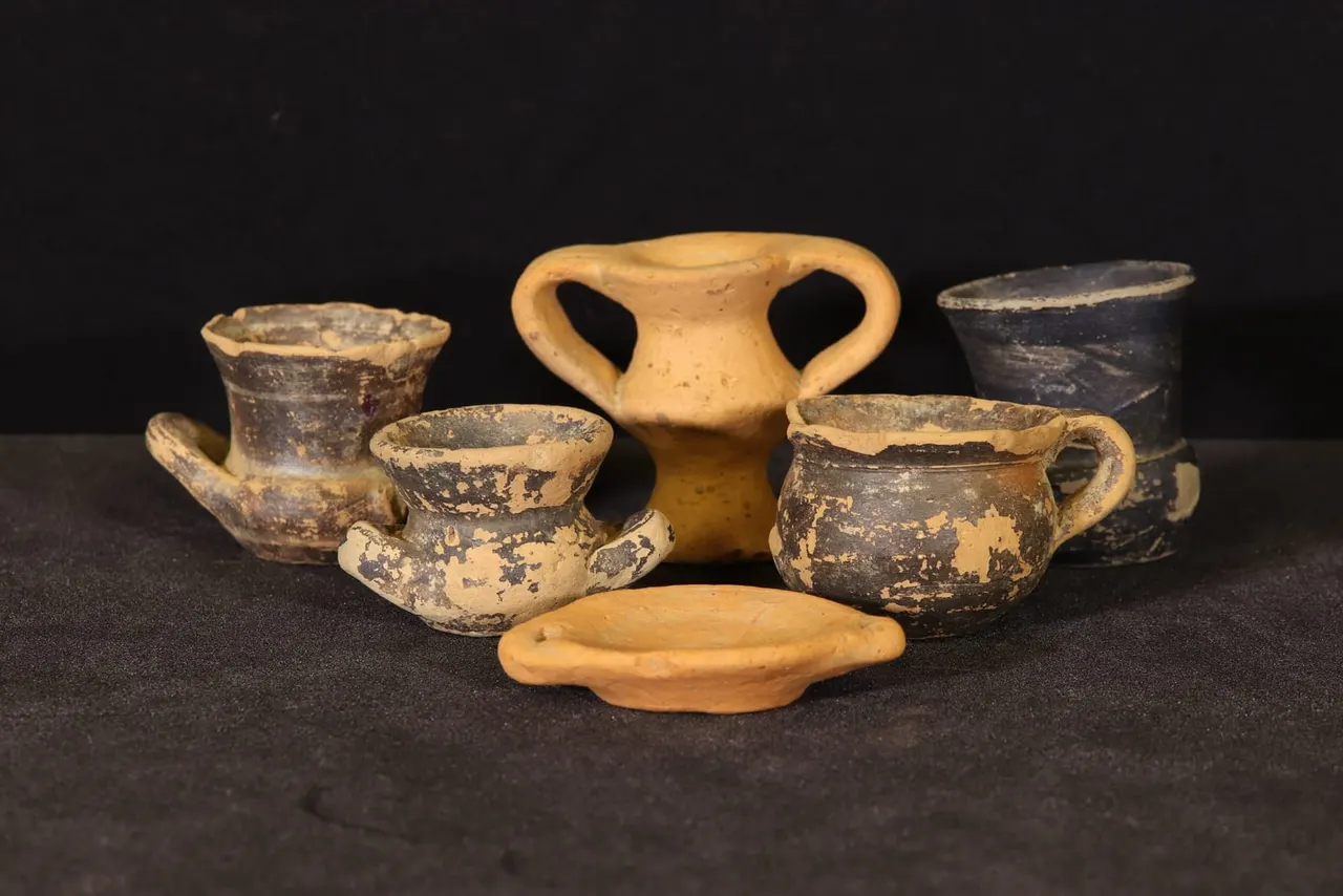Collection of ancient Greek terracotta vessels displayed against a black background, including bowls, handled cups, and a two-handled amphora.