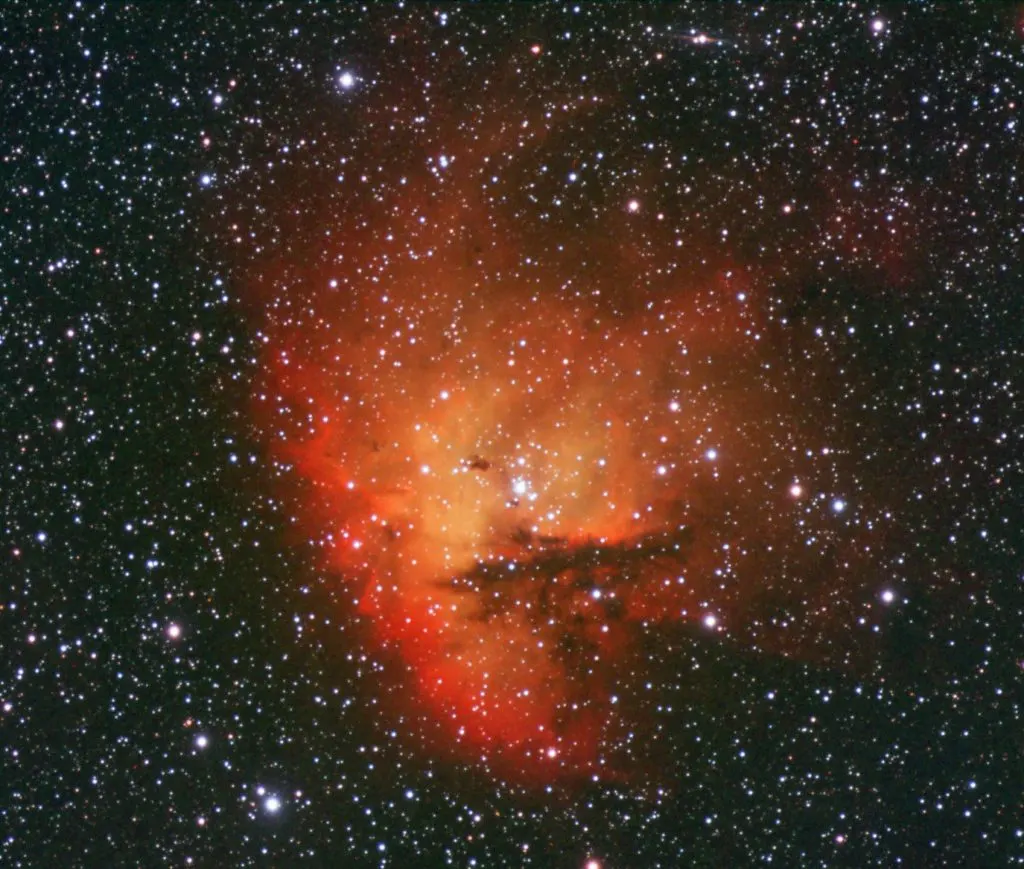 Astronomical photograph showing a red nebula surrounded by countless stars against a dark sky.