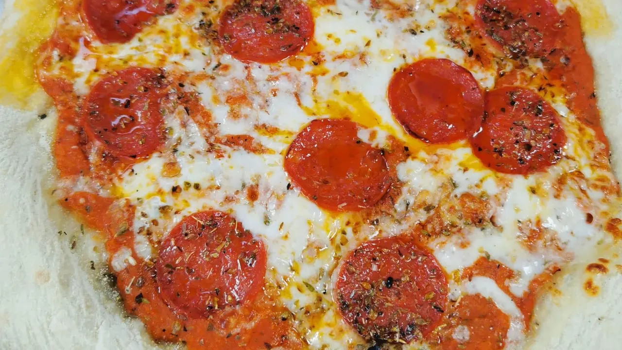 Pepperoni pizza with melted cheese and black pepper seasoning on a white plate.