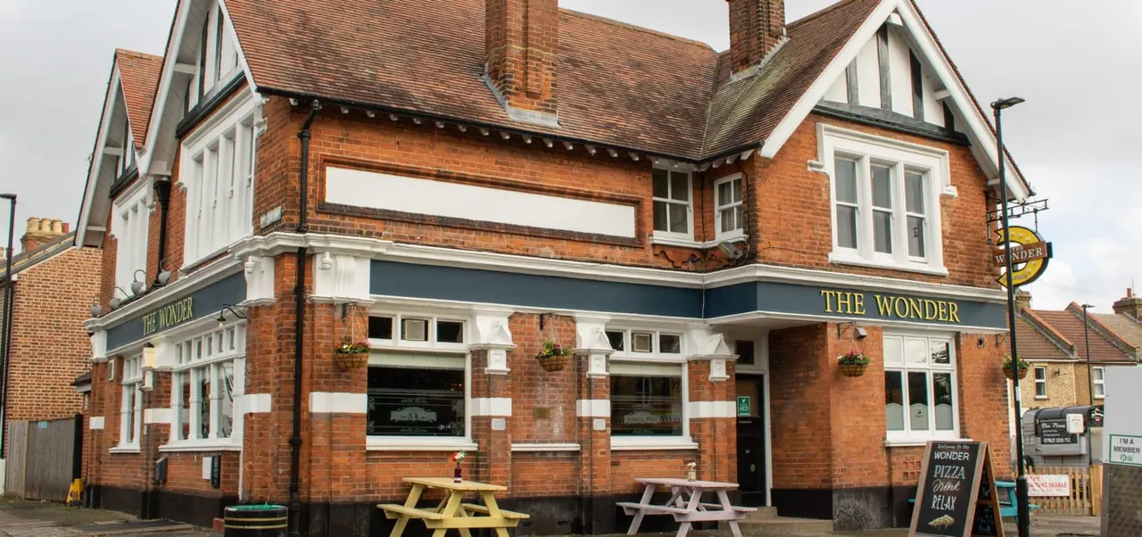 Victorian brick building with "The Wonder" pub frontage, picnic tables outside, and white-trimmed windows under a tiled roof.