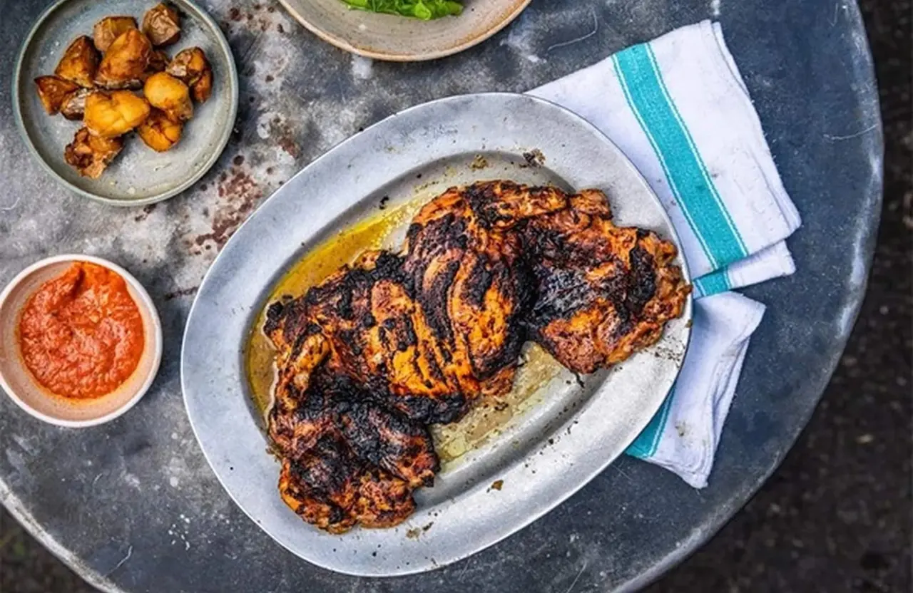 Charred grilled meat with roasted potatoes, red sauce and herbs on a slate table.
